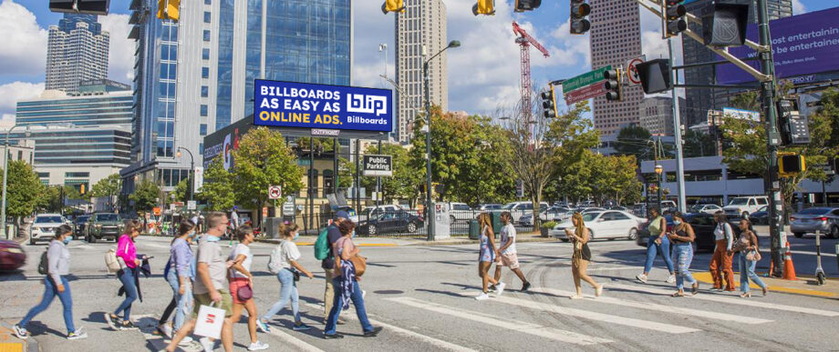 Busy city crosswalk with a Blip billboard overhead.